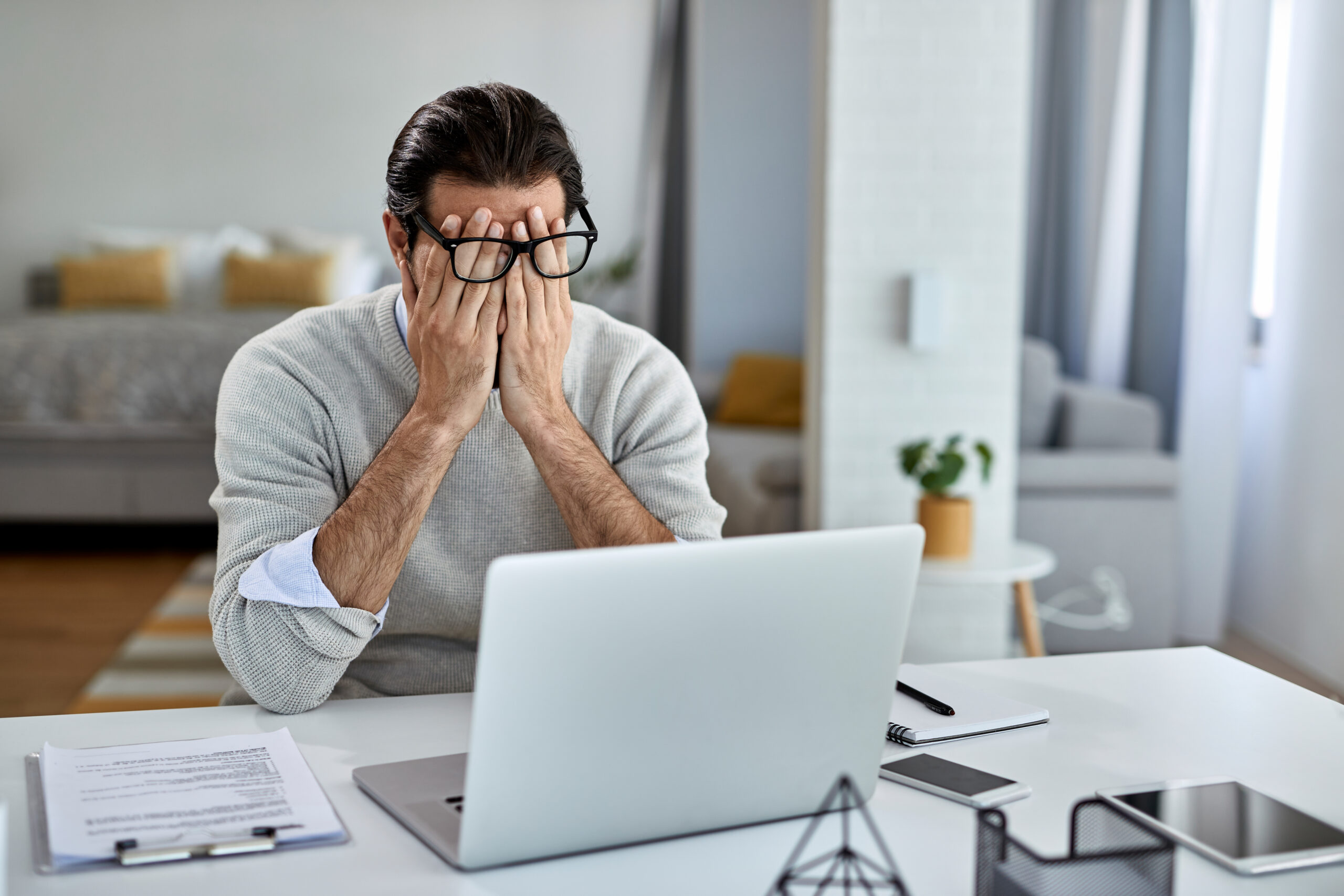 Businessman feeling exhausted after working on laptop at home.